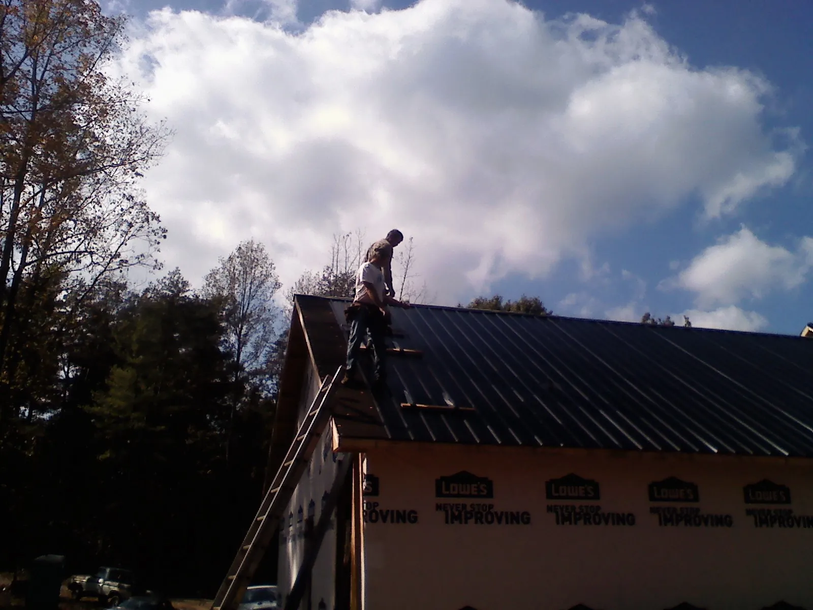 Roofer fastening dark metal panels high against a cloudy sky, from a Roof Inspection job in Summerville